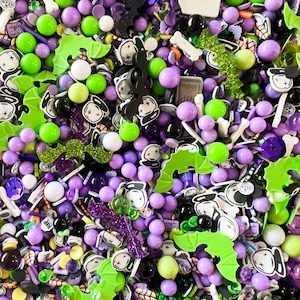 May include: A close-up of a variety of Halloween sprinkles in purple, green, and black. The sprinkles include bats, ghosts, and other Halloween-themed shapes.