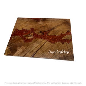 Op de afbeelding: Een vierkant houten snijplank met een rivier van rode hars in het midden. Het hout heeft een natuurlijk nerfpatroon met bruine en bruinachtige tinten. De tekst "AgraCraftShop" is rechtsonder zichtbaar.
