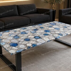 Könnte beinhalten: Ein rechteckiger Couchtisch mit einer Tischplatte aus zahlreichen kreisförmigen blauen und weißen Achat-Scheiben, die in einem Mosaikmuster angeordnet sind. Der Tisch wird von einem stabilen schwarzen Metallrahmen mit zwei U-förmigen Beinen getragen.