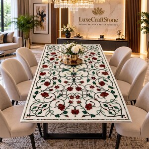 May include: A rectangular dining table with a white marble top featuring an intricate inlaid floral pattern in red and green stone. The table has a black metal base and is surrounded by six upholstered beige chairs in a dining room setting.