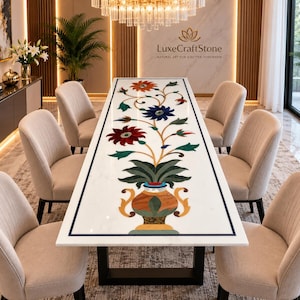 Puede incluir: Una mesa de comedor rectangular de mármol blanco con un diseño central incrustado de un jarrón colorido con tallos florales en rojo, azul, naranja y verde. La mesa tiene una base de metal negro y está rodeada por seis sillas tapizadas beige.