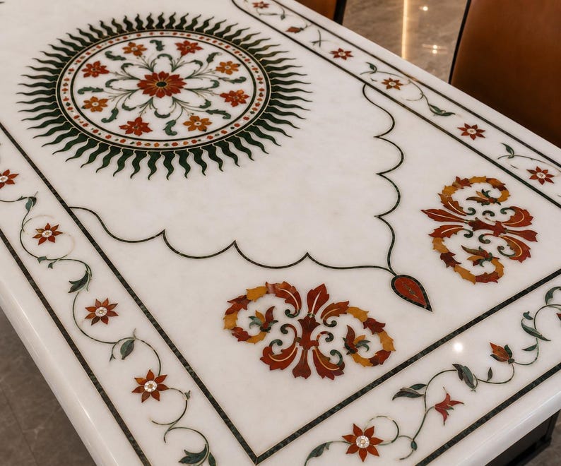 May include: A rectangular white marble tabletop featuring intricate floral inlay work. The design includes a central sunburst motif with red and orange flowers, surrounded by scrolling vine borders and symmetrical leaf patterns in red, orange, and green.