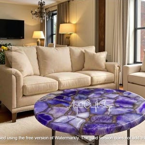 Puede incluir: Una mesa de centro redonda con una tapa de mosaico en tonos morados y blancos, ubicada en una sala de estar con un sofá color crema. La mesa tiene una base de metal oscuro. El texto "Agra Craft Shop" es visible en la mesa.