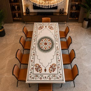 May include: A rectangular white marble dining table featuring an intricate inlaid floral pattern in shades of green, red, and orange, centred by a circular medallion design, surrounded by ten brown leather chairs with thin black metal frames.
