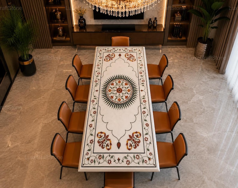 May include: A rectangular white marble dining table featuring an intricate inlaid floral pattern in shades of green, red, and orange, centred by a circular medallion design, surrounded by ten brown leather chairs with thin black metal frames.