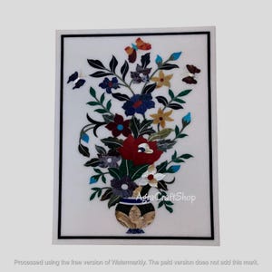Puede incluir: Una incrustación rectangular de mármol blanco con un diseño floral. El diseño presenta un jarrón lleno de flores y mariposas de colores. Las flores son rojas, azules, amarillas y blancas. La pieza está enmarcada con un borde negro.