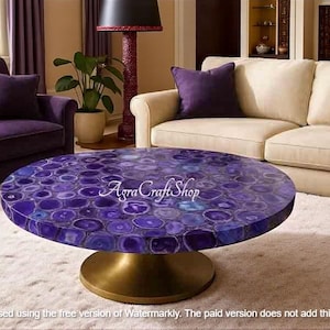 Könnte beinhalten: Ein runder Couchtisch mit einer polierten, lila Achatsteinplatte. Der Tisch hat einen goldfarbenen Sockel und steht in einem Wohnzimmer mit lila und cremefarbenen Möbeln. Der Text "Agra Craft Shop" ist auf dem Tisch zu sehen.