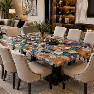 Può includere: Un tavolo da pranzo rettangolare con un piano composto da fette di pietra agata multicolore nelle tonalità del blu, verde acqua e ambra, sostenuto da una base a piedistallo nera, circondato da sei sedie imbottite beige con borchie.