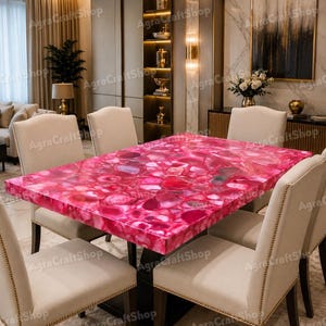 May include: A rectangular dining table featuring a polished surface made of vibrant pink agate stone slices. The table is supported by a dark base and is surrounded by six upholstered dining chairs with light beige fabric and nailhead trim.