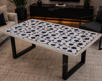 May include: A rectangular coffee table featuring a white surface inlaid with a repeating dark blue floral pattern and thin gold-toned lines. The table is supported by two black metal U-shaped legs. The text AgraCraftShop is visible on the image.