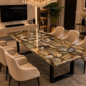 Puede incluir: Una mesa de comedor rectangular con una superficie pulida hecha de rodajas de piedra ágata translúcida multicolor en tonos marrón, crema y gris, sostenida por un marco de metal negro, rodeada por seis sillones tapizados en color beige.