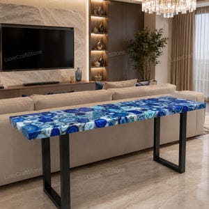 May include: A rectangular console table featuring a polished blue agate gemstone slab top with varied circular patterns in shades of navy, azure, and white. The tabletop is supported by two sturdy, black metal U-shaped legs positioned at each end.