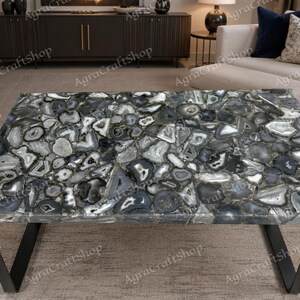 Könnte beinhalten: Ein rechteckiger Couchtisch mit einer Tischplatte aus zahlreichen polierten grauen, schwarzen und weißen Achat-Steinscheiben in einem Mosaikmuster, getragen von zwei schwarzen Metallbeinen mit kantigem V-förmigem Design.