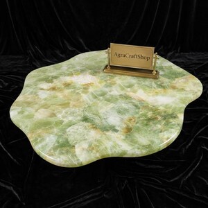 May include: A green onyx serving tray with a unique, organic shape. The tray has a polished surface with a mix of green, white, and brown tones. A small brass sign holder with the text "AgraCraftShop" is on the tray.