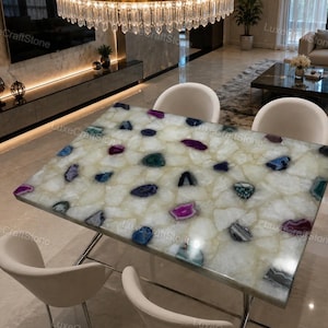 Puede incluir: Una mesa de comedor rectangular con una superficie pulida hecha de losas de piedra blanca translúcida incrustadas con varias rodajas de ágata multicolor en tonos púrpura intenso, azul y verde azulado, sobre un marco de metal con cuatro sillas.