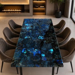May include: A rectangular dining table with a striking blue and black labradorite stone top. The table is supported by a black metal frame and surrounded by six gray upholstered chairs. The room features a fireplace and a modern design.
