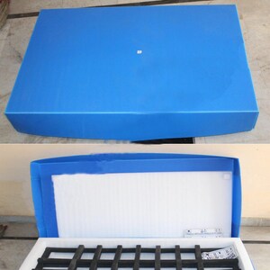 May include: A blue packing box with the text "PACKING BOX" in bold, white letters. The box is open, revealing a white interior with a black grid-like structure. The box is designed for shipping and storage.