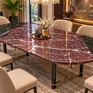May include: An oval dining table featuring a polished surface with a central section of deep burgundy marble and black marble ends, all accented by white veining. The table is supported by black cylindrical legs with gold-toned metal accents.