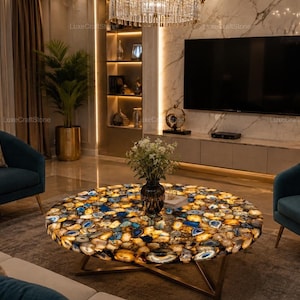 May include: A round coffee table featuring a surface made of multicolored agate slices in shades of blue, yellow, and white, supported by a gold-toned metal base, positioned between two dark teal upholstered armchairs in a living room.