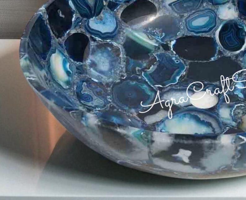 May include: A handcrafted, blue agate stone bowl with a mosaic design. The bowl features a variety of blue shades, from deep navy to light turquoise, creating a unique pattern. The text "Agra Craft" is visible on the side of the bowl.