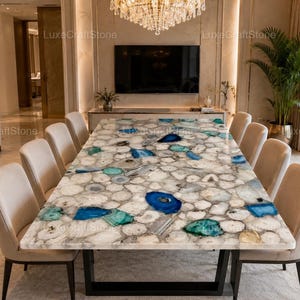 May include: A rectangular dining table featuring a surface made of white, grey, and translucent stone slices with prominent vibrant blue and teal agate accents. The table is supported by a black metal frame and surrounded by ten beige upholstered chairs.
