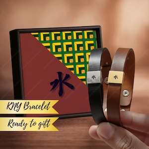 May include: Two leather bracelets, one black and one brown, each with a metal accent featuring a symbol. The bracelets are displayed with a decorative box with a geometric design and the text "KNY Bracelet Ready to gift."