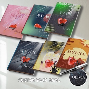 Op de afbeelding: Een verzameling gepersonaliseerde notitieboekjes met verschillende namen en ontwerpen. Elk notitieboekje heeft een uniek kleurenschema, een edelsteenillustratie en de tekst "CUSTOM YOUR NAME". Een pen met de naam "Olivia" is ook inbegrepen.