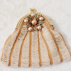May include: A vintage beaded purse with a gold-tone frame. The purse features cream-coloured beads arranged in vertical stripes, interspersed with gold-coloured accents. A floral embellishment with pearls and green leaves adorns the clasp.