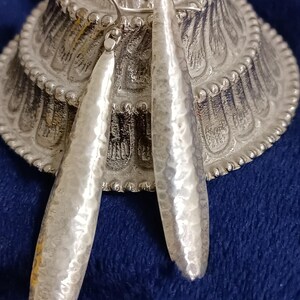 Pode incluir: Um par de brincos de prata pendentes com textura martelada. Os brincos são longos e estreitos, e têm um design simples e elegante.