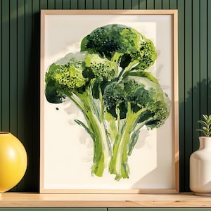 Könnte beinhalten: Ein gerahmter Aquarelldruck von Brokkoli. Das Kunstwerk zeigt eine Nahaufnahme von drei Brokkoliköpfen mit grünen und weißen Farbtönen. Der Druck wird auf einer Holzoberfläche mit dekorativen Vasen und einer gelben Kugel ausgestellt.