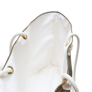 May include: White tote bag with rope handles and gold-colored grommets. The bag's interior is white, and the exterior features a nature-inspired design. The rope handles are thick and sturdy, providing a comfortable grip for carrying.