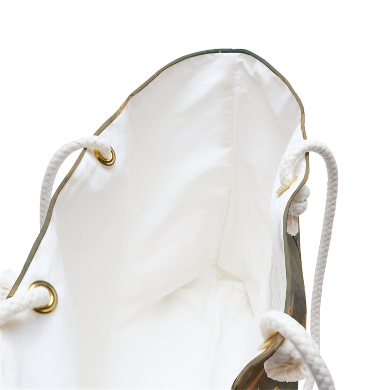May include: White tote bag with rope handles and gold-colored grommets. The bag's interior is white, and the exterior features a nature-inspired design. The rope handles are thick and sturdy, providing a comfortable grip for carrying.