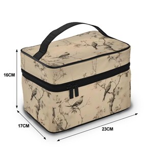Op de afbeelding: Een beige make-uptas met een zwarte handgreep en ritssluiting. De tas heeft een vogel- en bloemenontwerp. De tas is 23 cm lang, 17 cm breed en 16 cm hoog.