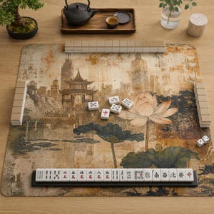 May include: A mahjong set featuring a rectangular play mat with a printed illustration of a traditional pavilion, lotus flowers, and city buildings. The set includes white tiles with black and red characters, a tile rack, and two small white dice.