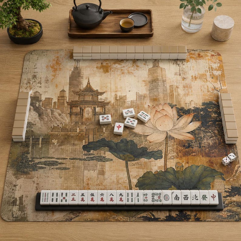 May include: A mahjong set featuring a rectangular play mat with a printed illustration of a traditional pavilion, lotus flowers, and city buildings. The set includes white tiles with black and red characters, a tile rack, and two small white dice.