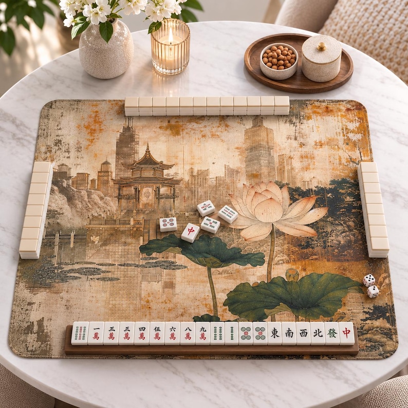 May include: A rectangular mahjong mat featuring a printed landscape of a traditional pavilion and a large lotus flower in shades of gold, brown, and green. The mat is surrounded by white mahjong tiles, with a wooden rack holding a row of tiles.