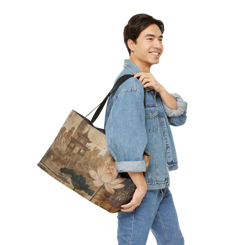 May include: A large tote bag featuring a sepia-toned Asian-inspired design. The artwork includes a pagoda, lotus flower, and other traditional elements. The bag has a black strap and is carried over the shoulder.