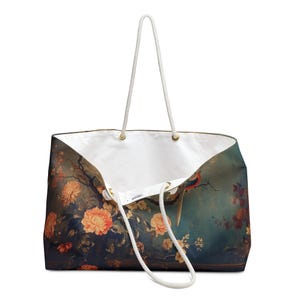 May include: Large tote bag with a floral and bird design. The bag features a white interior and rope handles. The exterior has a dark teal background with orange flowers and a bird with red, blue, and green feathers.