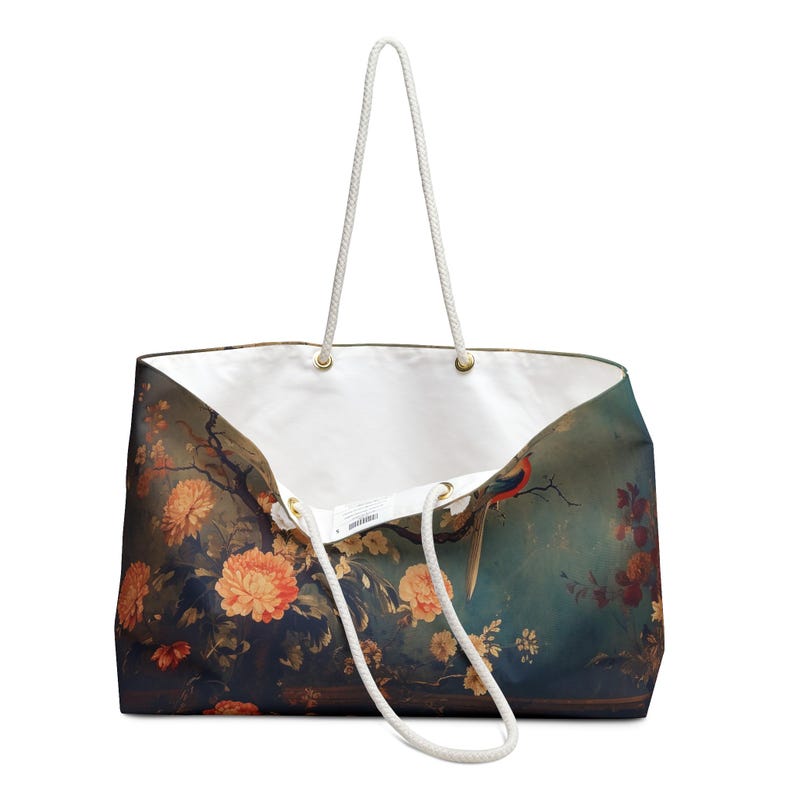 May include: Large tote bag with a floral and bird design. The bag features a white interior and rope handles. The exterior has a dark teal background with orange flowers and a bird with red, blue, and green feathers.