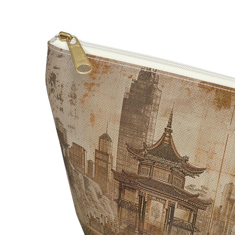 May include: A beige zippered pouch featuring a sepia-toned illustration of a cityscape with a pagoda and skyscrapers. The pouch has a gold-colored zipper and a cream-colored interior lining. The design gives the pouch a vintage aesthetic.