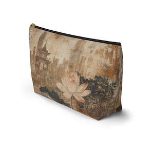 May include: A beige zippered pouch featuring a vintage-style illustration of a lotus flower and a pagoda. The design includes a cityscape and dark accents, with a black zipper and trim.