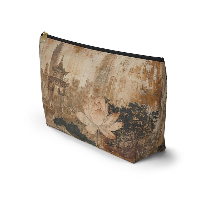 May include: A beige zippered pouch featuring a vintage-style illustration of a lotus flower and a pagoda. The design includes a cityscape and dark accents, with a black zipper and trim.