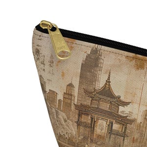 May include: A beige zippered pouch featuring a vintage-style illustration of a pagoda and city skyline. The design is in shades of brown and tan, with a gold-colored zipper and black trim. The pouch is likely made of canvas or a similar fabric.