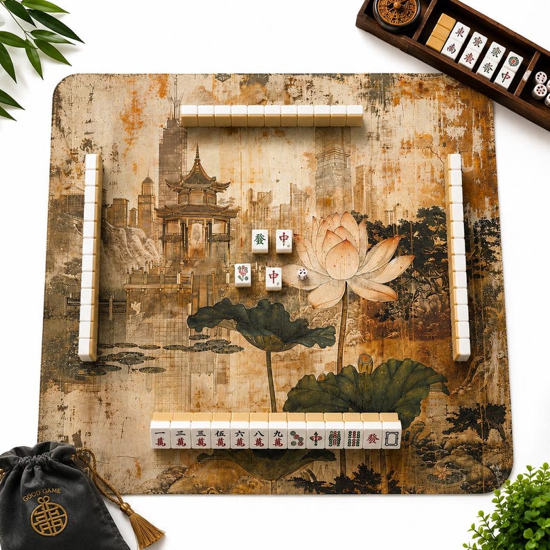 May include: A square mahjong mat featuring a sepia-toned illustration of a traditional pagoda and a large lotus flower. The mat is arranged with white mahjong tiles in rows, a wooden tile rack, a small die, and a black drawstring storage bag.