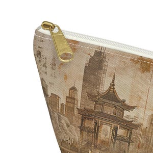 May include: A beige zippered pouch featuring a vintage-style illustration of a pagoda and city skyline. The pouch has a gold-colored zipper pull with the brand name "ZOKY" embossed on it. The design is printed on a textured fabric.