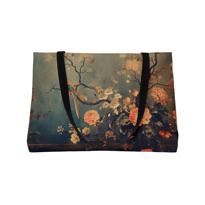 May include: A tote bag featuring a vintage-style floral and bird design. The bag has a teal background with peach and cream-colored flowers and a colorful bird. It has black straps and a rectangular shape.