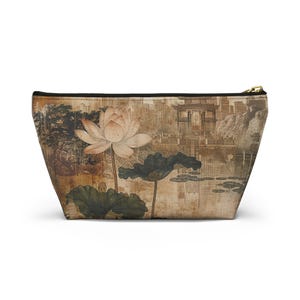 May include: A beige cosmetic bag featuring a vintage-style illustration of a lotus flower, lily pads, and a traditional Asian landscape. The bag has a black zipper and a gold-colored zipper pull.