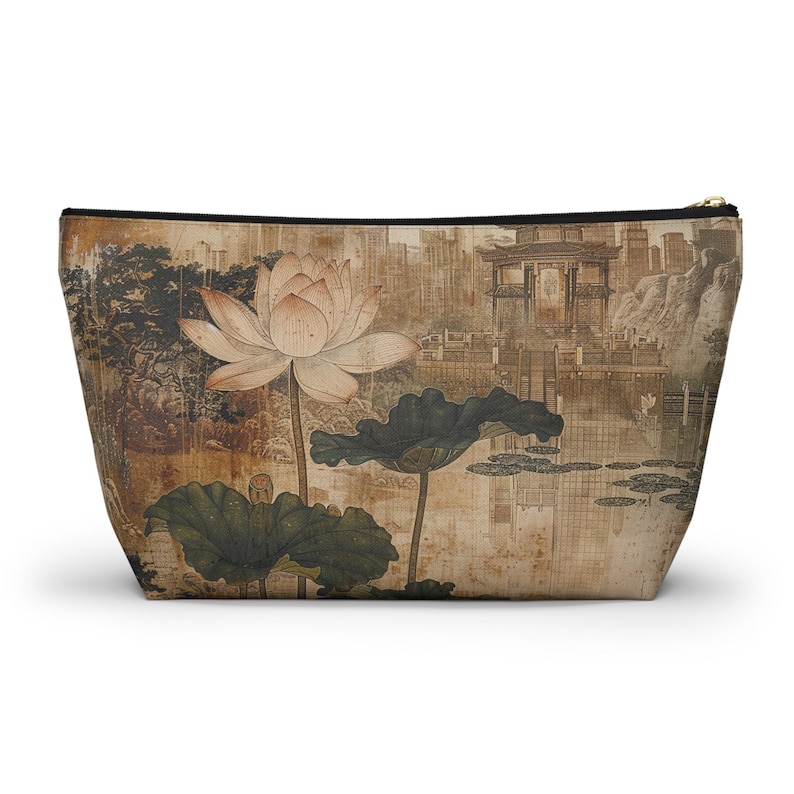 May include: A beige cosmetic bag featuring a vintage-style illustration of a lotus flower and leaves. The artwork includes a background of a traditional Asian landscape with buildings and water. The bag has a black zipper.