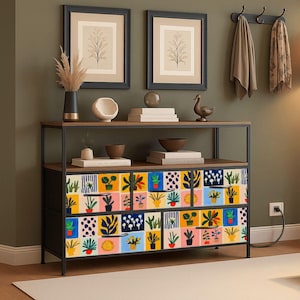 May include: A contemporary console table with a black metal frame and a wooden top and shelf. The cabinet doors display a vibrant, patterned design of potted plants. Two framed botanical prints are above the table.
