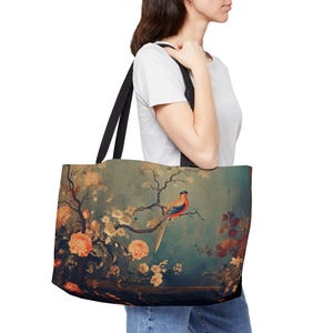 May include: A large tote bag with black straps featuring a vintage-style painting of a bird perched on a branch with flowers. The artwork has a teal background with orange, red, and yellow floral accents.